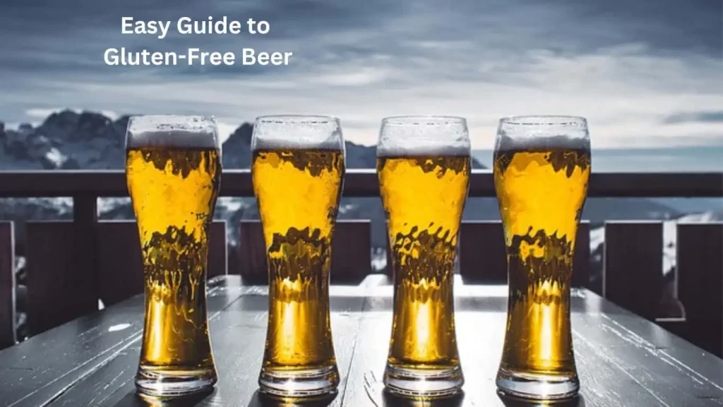 Four glasses of golden beer are lined up on a wooden table, set against a backdrop of mountains and a cloudy sky.