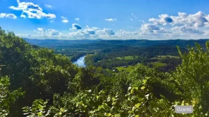 Scenic view of the Ozark Mountains near Eureka Springs, Arkansas, featuring lush green hills, a winding river, and a bright blue sky.