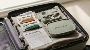 Gluten-free travel essentials packed in a carry-on suitcase, including gluten-free snacks, a celiac disease dining card, reusable utensils, and food containers for celiac-safe travel.